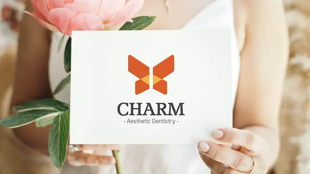 Charm Aesthetic dentistry logo design featuring a stylized butterfly symbol with warm colors and balanced geometry paired with elegant typography